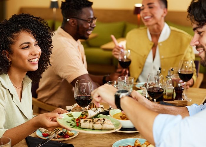 A Group Of People Sitting At A Table With Wine Glasses